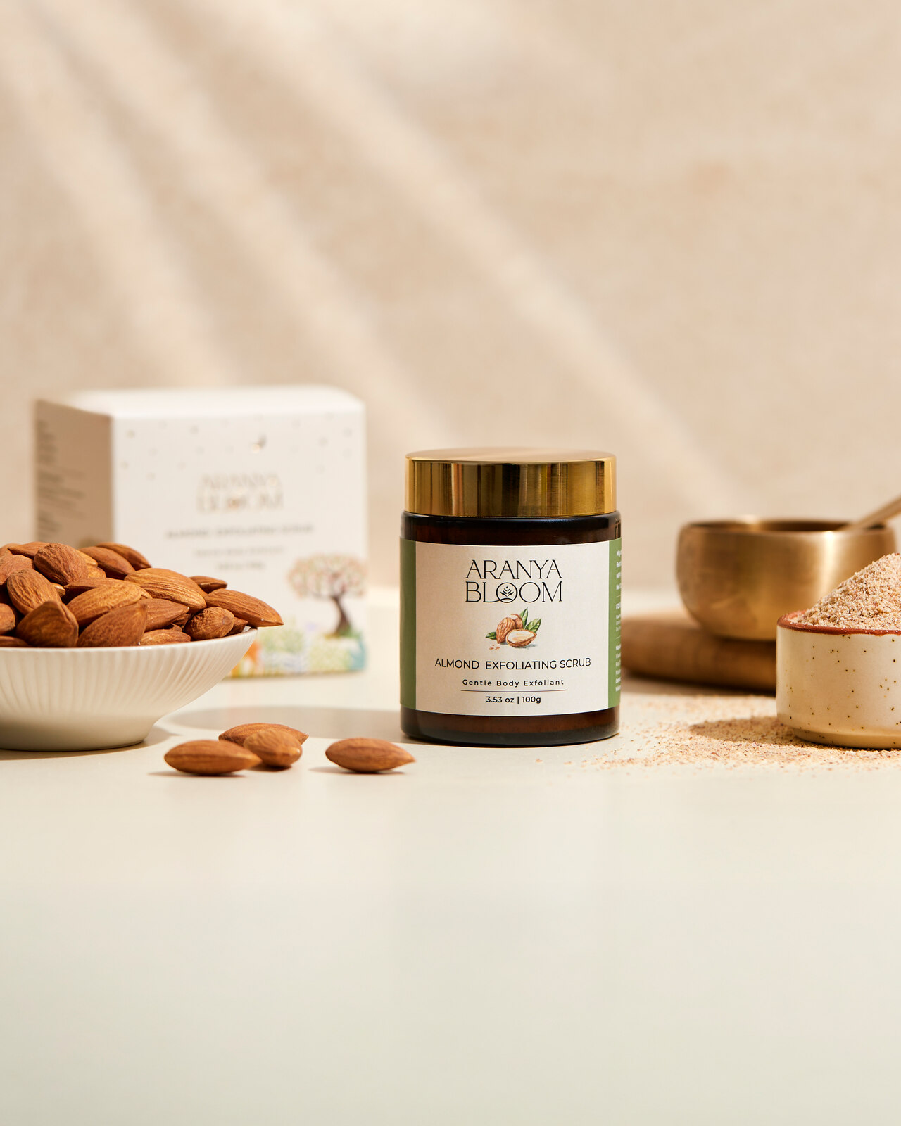 Aranya Bloom Almond Scrub jar and carton on a warm neutral surface.